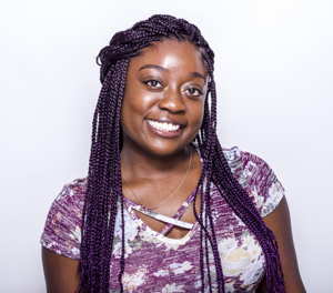 A Black woman with long hair smiles in front of a neutral background