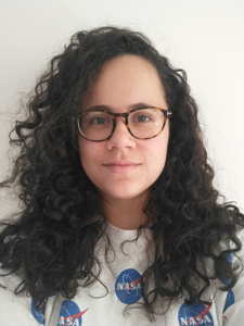 A smiling person with long curly hair, glasses, and a NASA t-shirt
