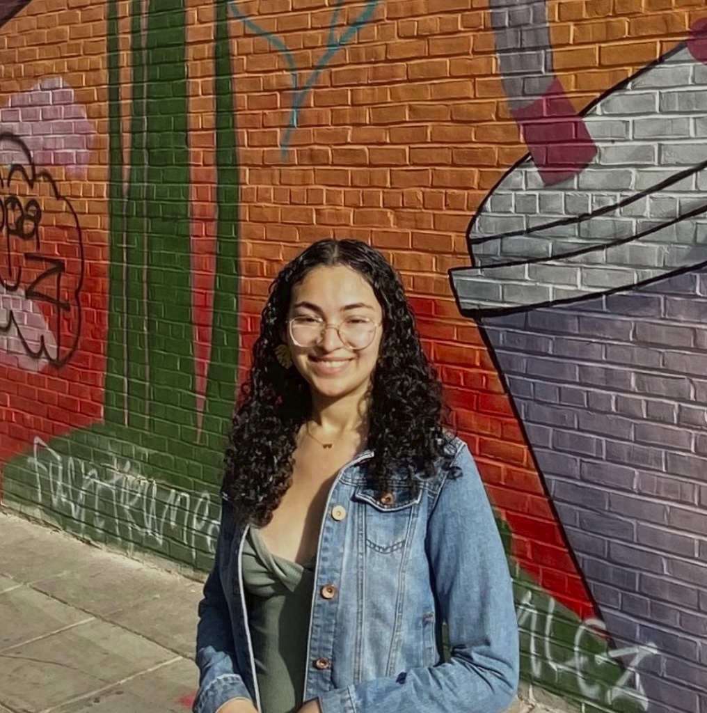 picture of Karina wearing glasses and smiling, standing in front of street art