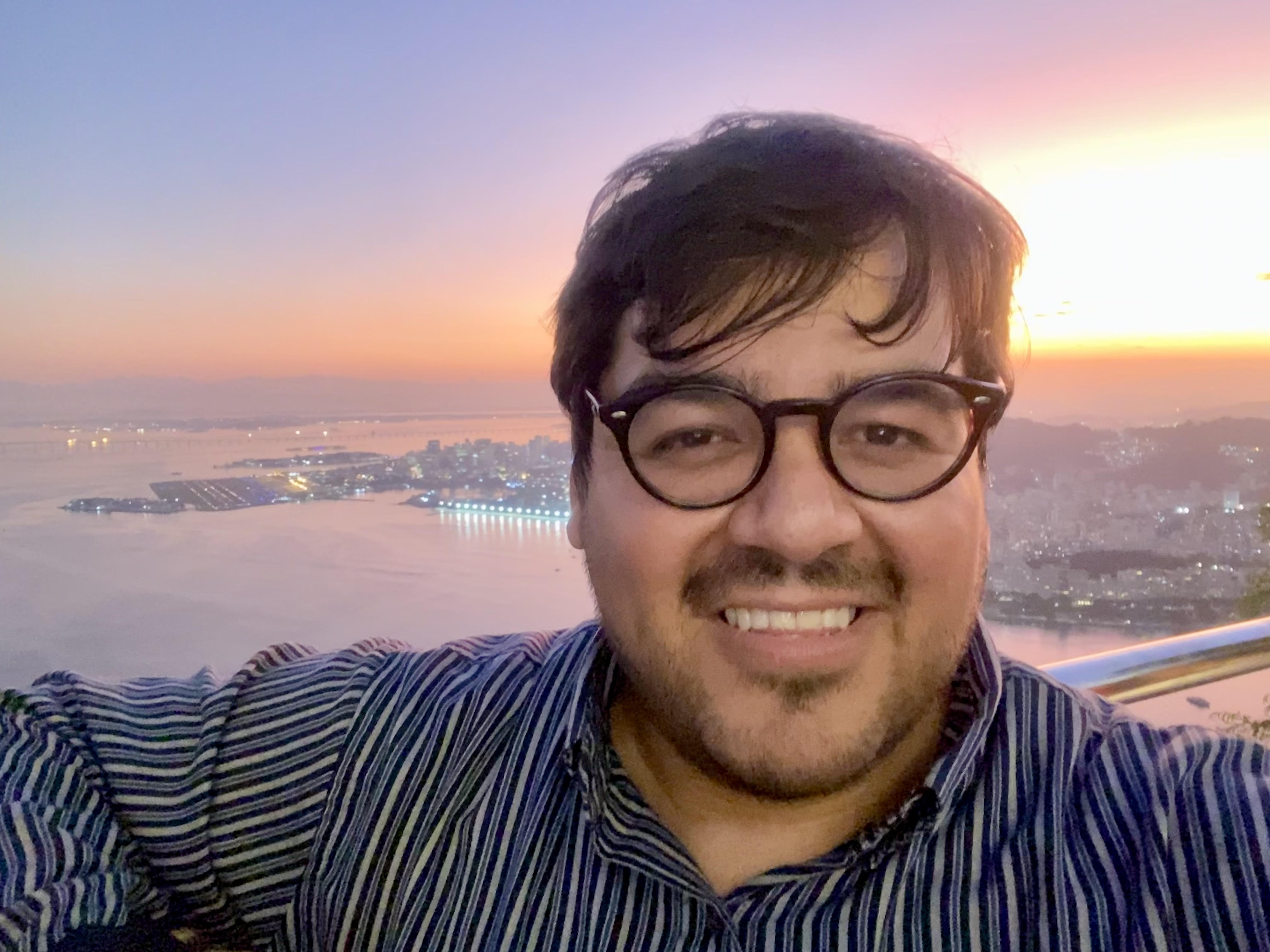 Andy smiling, wearing a striped button-down shirt and glasses