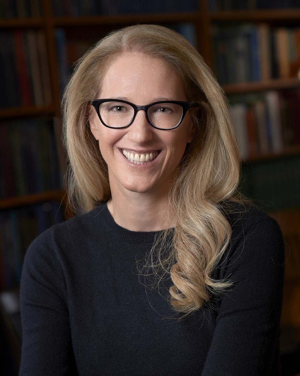 Image of Raina Plowright, smiling, wearing black shirt and black glasses.