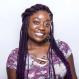 A Black woman with long hair smiles in front of a neutral background